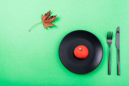 Halloween table setting with black plate, decorative pumpkin and autumn leaf on green table. Top view, flat lay.の写真素材