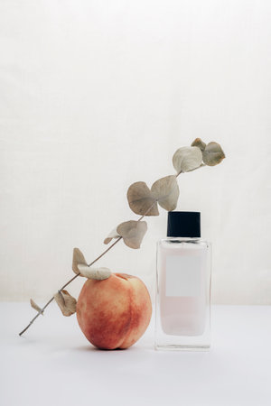 Cosmetic bottle, peach fruit and eucalyptus branch on white table. Beauty, fashion concept. Front view.の写真素材
