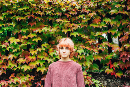 Beautiful teenage girl with pink hair standing against colorful fall foliage background.の写真素材