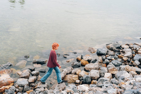Beautiful teenage girl with red hair walking along the rocky river bank.