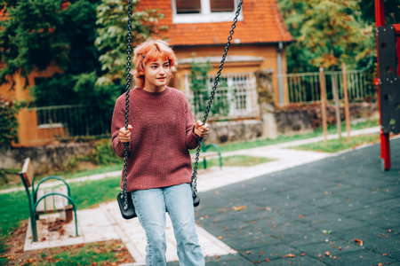 Beautiful teenage girl with red hair swinging on swings. Healthy lifestyle concept.の写真素材