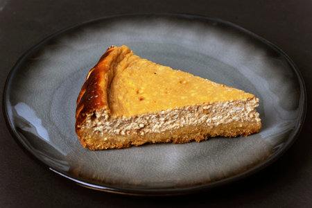 Homemade cheesecake on a gray plate on black table, closeup.の写真素材