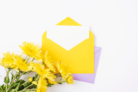 Yellow envelope with blank card and flowers on white background. Birthday, invitation, holiday concept. Top view, flat lay, mockup.の写真素材