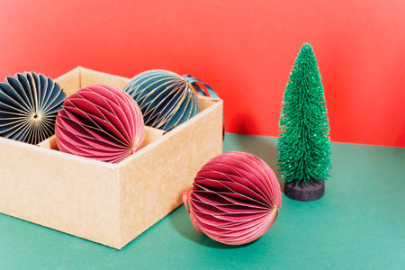 Christmas paper balls in a box and fir tree toy on red and green background. New year concept. Closeup.の写真素材