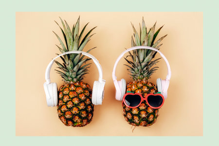 Two pineapples in sunglasses with headphones on light green and yellow background. Summer concept. Top view, flat lay.の写真素材