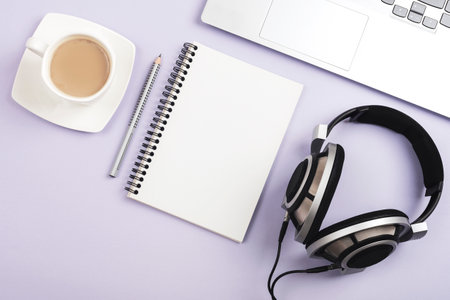 Notepad, coffee cup, laptop and headphones on lilac background. Top view, flat lay, mockup.の写真素材