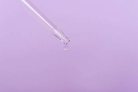 Drop of cosmetic face serum on a pipette on light purple background. Front view, closeup. Copy space.の写真素材