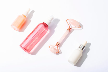 Pink cosmetic bottles, facial roller on white background with sharp shadows. Natural cosmetics, skin care concept. Top view.の写真素材