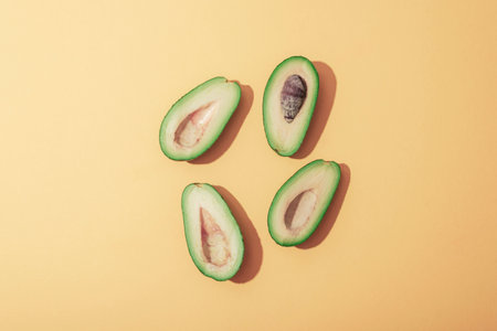 Halves of avocado on yellow background with sharp shadows. Healthy vegan food concept. Top view, flat lay.の写真素材
