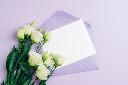 Eustoma grandiflorum white flowers and envelope with blank card on purple background, mockup. Festive background, flat lay, copy space.の写真素材