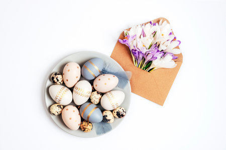 Gray plate with painted Easter eggs and envelope with crocus flowers on white background. Easter greeting card. Top view, flat lay.の写真素材