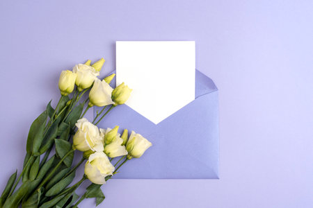 Envelope with blank card and white eustoma flowers on purple background. Valentines day, Mothers day, Womens day concept. Top view, flat lay, mock up.の写真素材