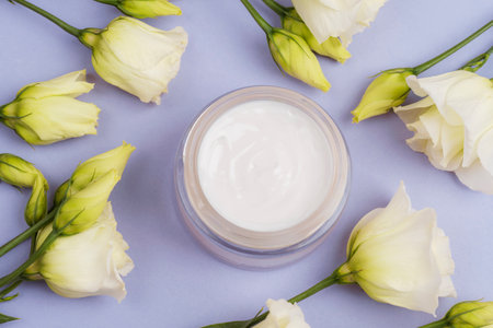 Cosmetic cream jar and white eustoma flowers on purple background. Top view, flat lay.の写真素材