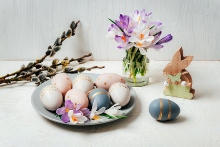 Gray plate with painted Easter eggs and wooden toy bunny, crocus flowers on white table. Easter greeting card.の写真素材