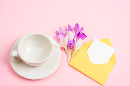 Empty coffee cup, bouquet of spring flowers and envelope with blank card. Top view, mockup.