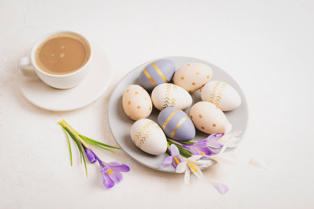 Gray plate with painted Easter eggs, coffee cup and crocus flowers on white background. Easter concept. Top view.の写真素材