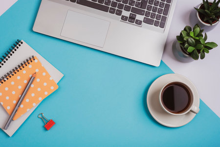 A cup of coffee, laptop computer, notepads, pencil and succulent plants on blue background. Cozy workplace, work from home concept. Top view, flat lay, copy spaceの写真素材