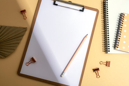 Desktop with blank clipboard, notepad, fan leaf and pencil with light and shadow. Top view, flat lay, mockup.の写真素材
