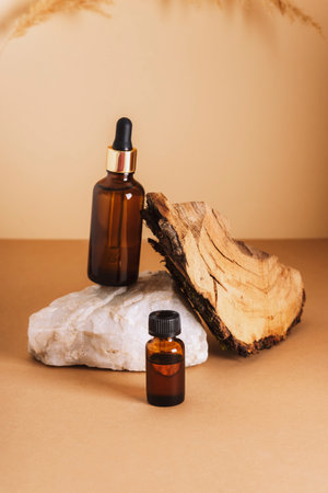 Brown cosmetic serum and essential oil bottles on a stone podium and wooden bark on neutral background. Natural skin care cosmetics concept. Closeup.の写真素材