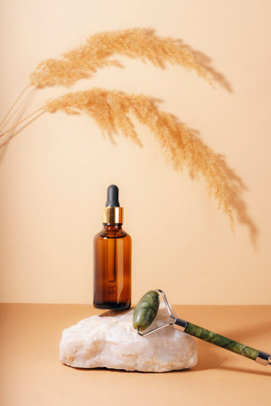 Brown cosmetic serum bottle and jade facial roller on a natural stone podium. Natural skin care cosmetics concept. Closeup.の写真素材