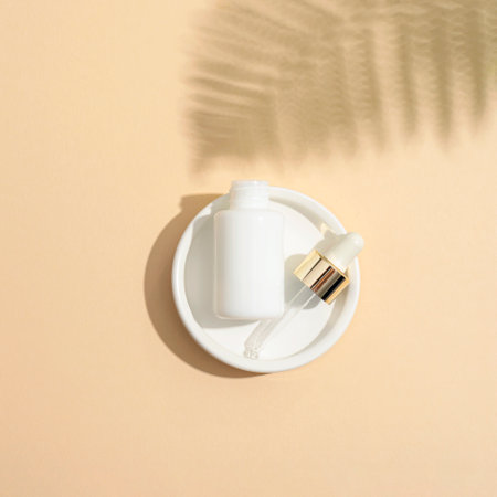 White dropper bottle with pipette and fern leaf shadow on beige background. Natural anti-aging cosmetics concept. Top view, flat lay, mockup.の写真素材