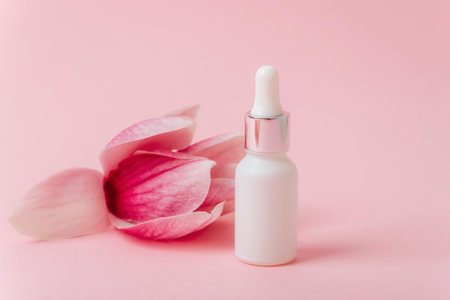 Cosmetic white serum bottle on pink background with magnolia flower. Mock up, copy space.の写真素材
