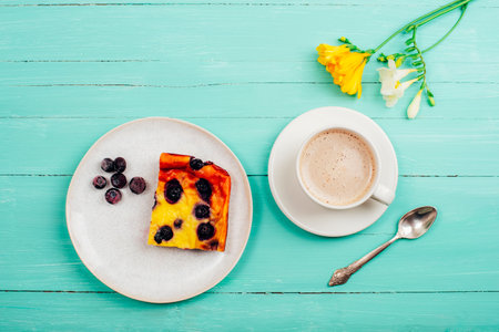 A cup of coffee and blueberry cake, yellow freesia flower on turquoise wooden table. Top view, flat lay.の写真素材