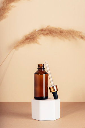 Brown cosmetic serum bottle on a podium and pampas grass on beige background. Natural skin care cosmetics concept. Closeupの写真素材