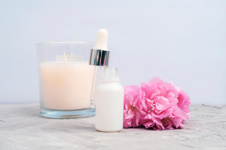 White serum dropper bottle, pink cherry blossom and aroma candle on concrete background. Closeup, front view.の写真素材