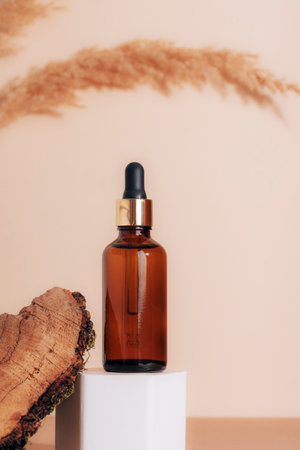Brown cosmetic serum bottle on a podium and wooden bark, pampas grass decoration. Natural skin care cosmetics concept. Closeup.の写真素材