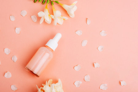 Cosmetic serum bottle and white freesia flowers on coral pink background. Top view, flat lay, copy space.の写真素材