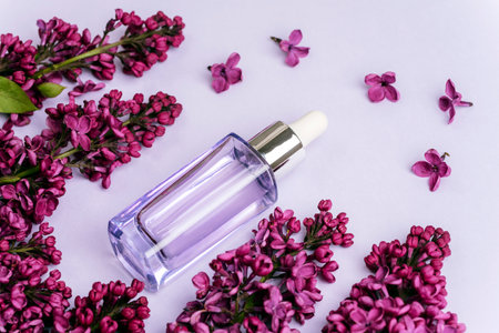 Serum bottle and lilac flowers on light purple background. Natural cosmetics, skin care concept. Top...