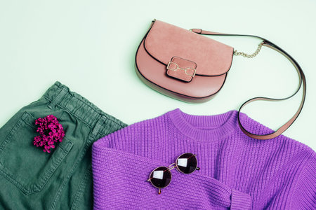 Stylish woman's outfit: purple sweater, green jeans, sunglasses and handbag. Lilac flowers decoration. Top view, flat lay.の写真素材