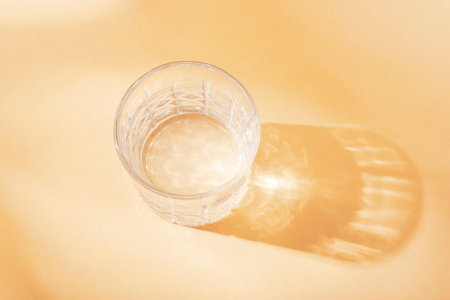 A glass with water in sunlight on neutral beige background, top view.の写真素材