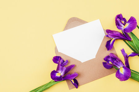 Envelope with blank paper and blue iris flowers on yellow table. Top view, flat lay, mockup.の写真素材