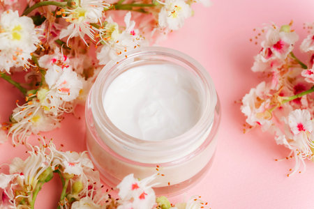 White cream jar with Horse chestnut flowers on pink background. Natural organic cosmetics concept. Top viewの写真素材