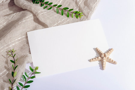 Blank paper sheet, starfish and green leaves on white table. Top view, flat lay, mockup.の写真素材