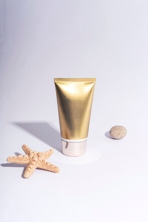 Golden cream tube and starfish on white background with hard shadows. Sunscreen, natural cosmetics concept. Closeup.の写真素材