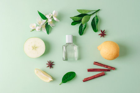 Perfume bottle and apple, lemon fruits, jasmine flowers, star anise and cinnamon sticks on light green background. Top view, flat lay.の写真素材