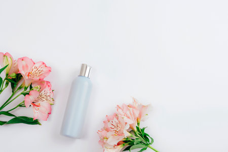 Blue cosmetic bottle and Alstroemeria pink flowers on white background, flat lay, top view. Blank label for branding, mockup. Natural organic eco cosmetics. Copy space.の写真素材