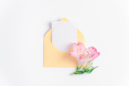 Yellow envelope with blank card and pink alstroemeria flower on white background. Birthday, Valentines day, Mothers day, Womens day concept. Top view, flat lay, mock upの写真素材