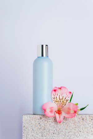 Cosmetic facial cleanser bottle and alstroemeria pink flower on natural stone podium, closeupの写真素材