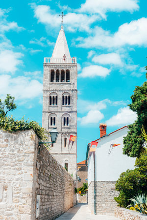 Bell tower of St. Marys church against blue sky and narrow street of the old town of Rab on the island Rab, Croatiaの写真素材