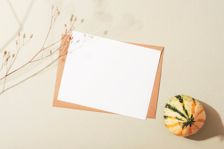 Envelope with blank card, dried flower and small pumpkin with sharp shadows on neutral background. Autumn concept. Top view, flat lay, mockupの写真素材