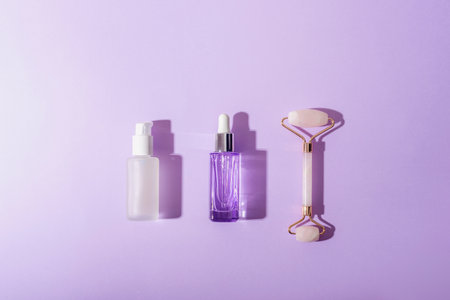 Cosmetic serum dropper bottles, rose quartz crystal facial roller on purple background. Skincare, spa and wellness concept. Top view, flat lay.の写真素材
