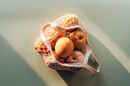 Fresh ripe peaches in a string bag in sunlight. Zero waste concept, healthy food. Top view, flat lay.の写真素材