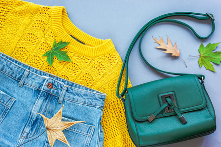 Flat lay of womans yellow sweater, jeans, green bag and autumn leaves on grey background. Autumn fashion concept. Top view, flat layの写真素材