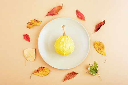 Autumn table place setting with grey plate with pumpkin and yellow leaves on neutral background. Thanksgiving, halloween decoration. Top view, flat lay.の写真素材