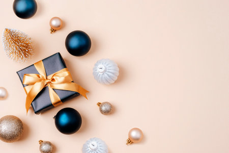 Black gift box with golden ribbon and Christmas baubles on beige background. Top view, flat lay, copy spaceの写真素材