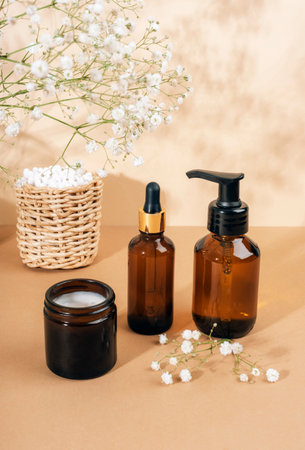 Cosmetic face cleanser, serum brown glass bottles, cream jar and gypsophila white flowers on light beige background. Natural cosmetics, spa and wellness concept. Closeup.の写真素材